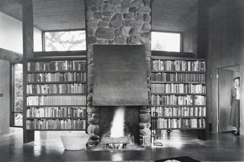 Black and White photo of the fireplace and side book shelves. Esther looks on from kitchen doorway.