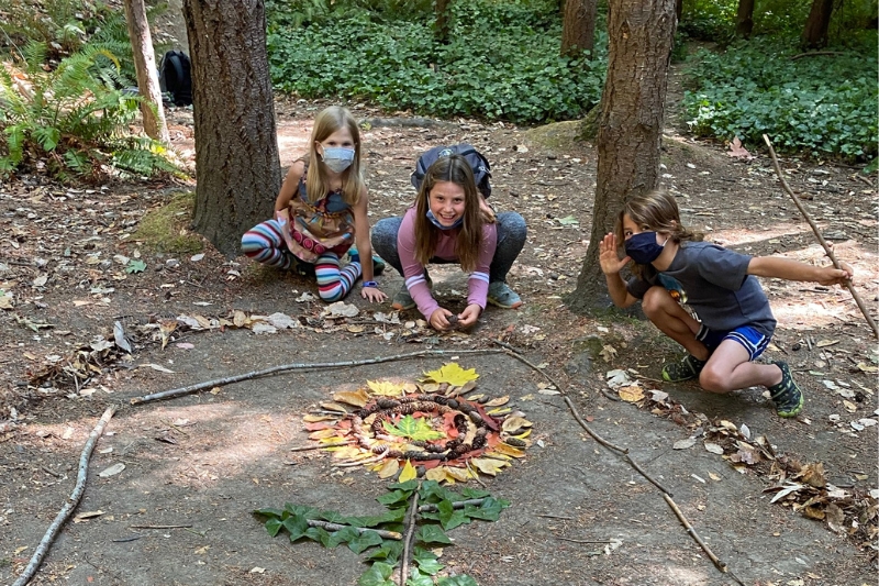 Three kids smiling next to their nature art from summer camp 2022